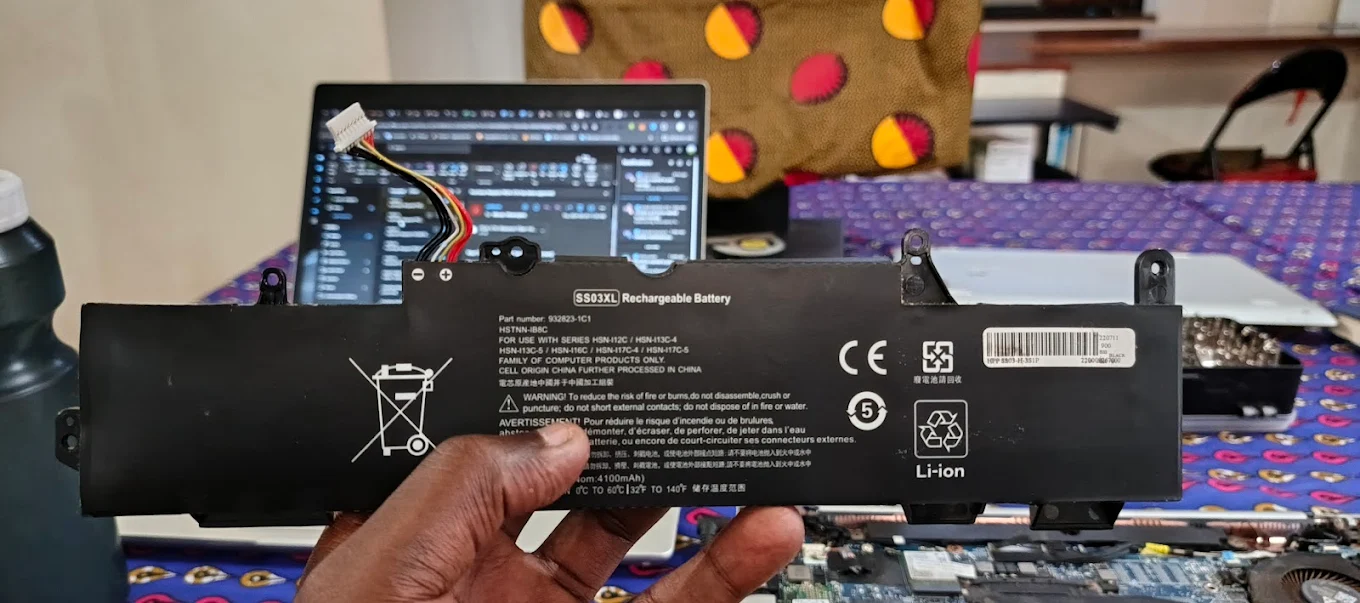 Replacement laptop battery held in front of a repair workspace